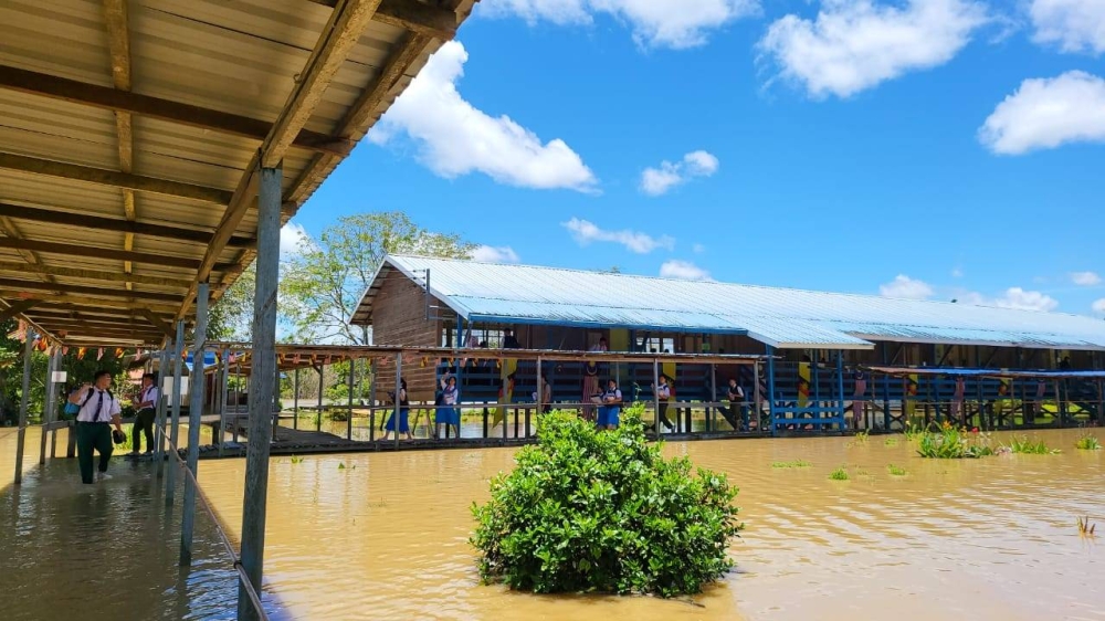 Students brave floodwaters to attend school at SMK Tutoh Apoh this morning. — Borneo Post pic