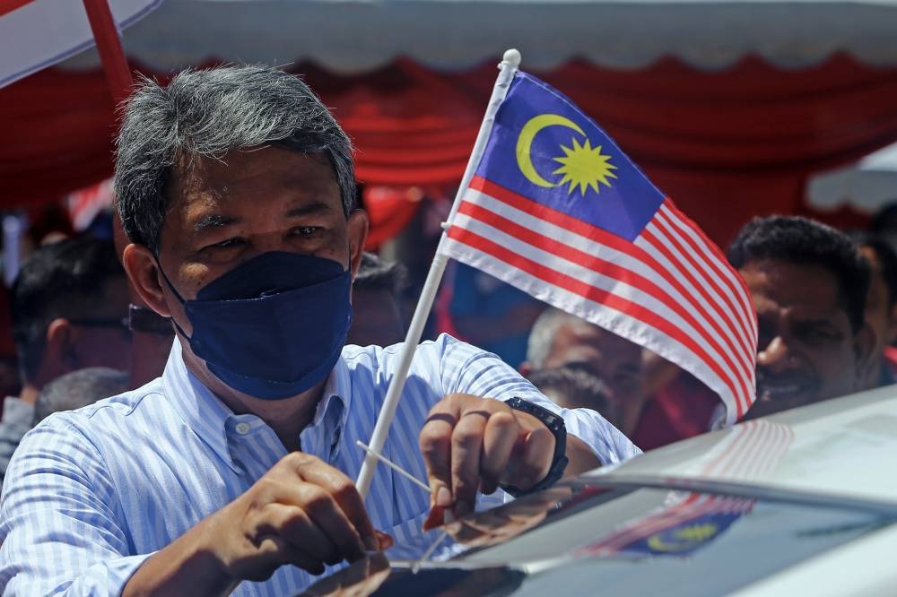 Datuk Seri Mohamad Hasan fixes a Jalur Gemilang on a car at the Merdeka@Komuniti DUN Paroi 2022 programme at Dataran Senawang, Seremban, September 14, 2022. — Bernama pic    
