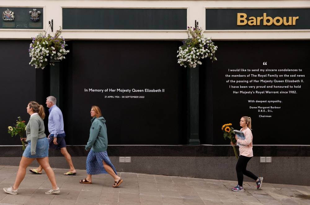 People walk past a condolence message displayed outside a Barbour shop, following the passing of Britain's Queen Elizabeth, in Windsor, Britain September 11, 2022. — Reuters pic