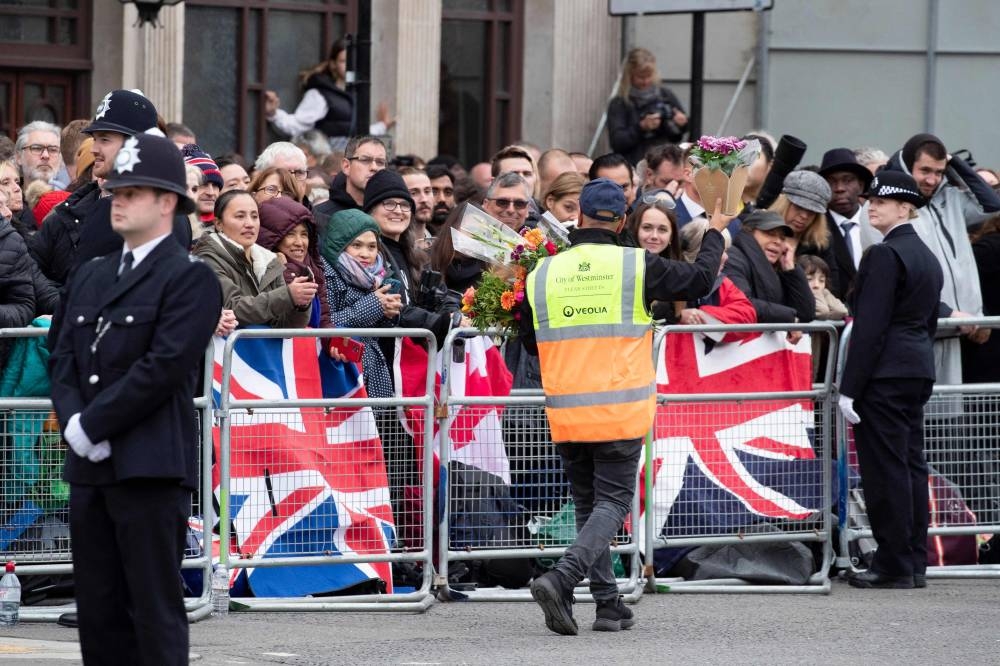 A Westminster council worker gestures to the crowd with a bunch of flowers as well-wishers gather around Parliament Square ahead of the State Funeral of Queen Elizabeth II in London on September 19, 2022. — Joshua Bratt/Pool/AFP pic