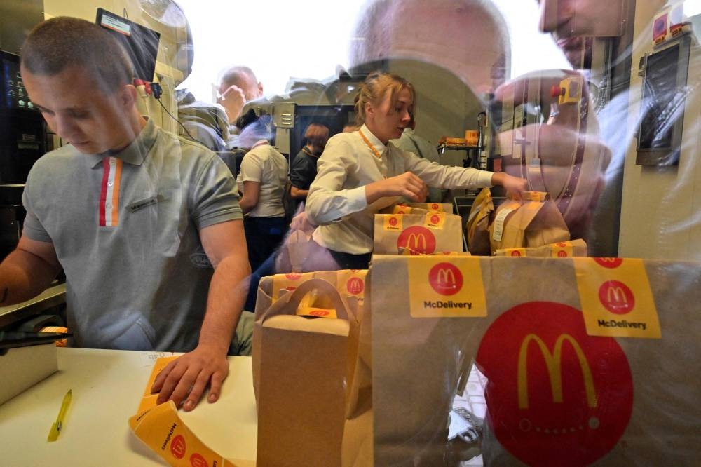 A photographer is reflected on a window as employees of a McDonald restaurant prepare the orders in Kyiv on September 20, 2022 after the US fast-food giant starts to reopen in the Ukrainian capital amid the Russian invasion of Ukraine. — AFP pic