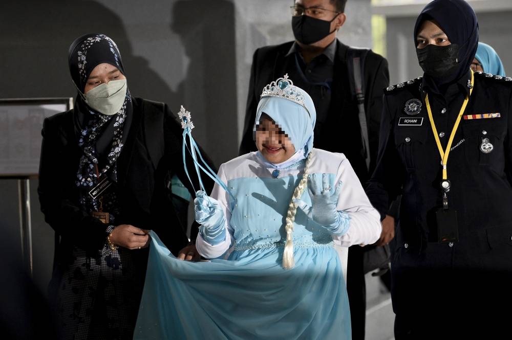 Bella, in a blue dress like the one worn by Elsa in ‘Frozen’, was seen smiling when she arrived at the Kuala Lumpur Court Complex around 9am accompanied by JKM officers and policemen. September 22, 2022. — Bernama pic 