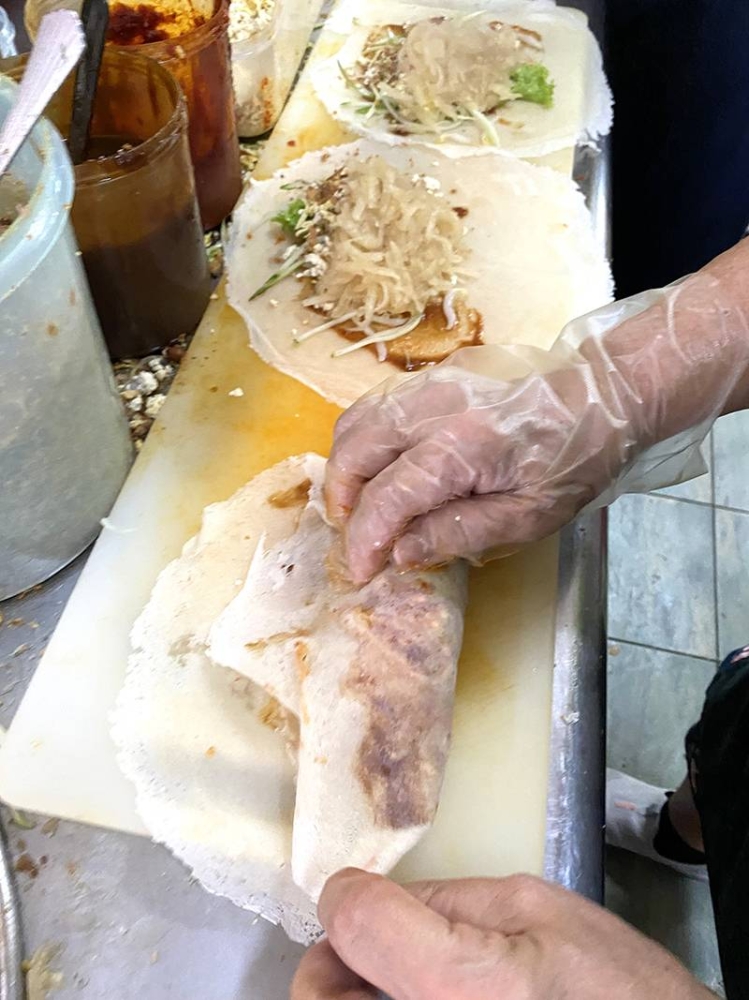 Once each layer is added, the 'popiah' is slowly rolled together.