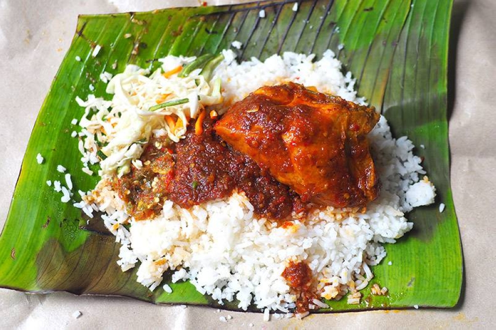 The meals are served on brown paper, like this 'nasi berlauk' with 'ayam masak merah.