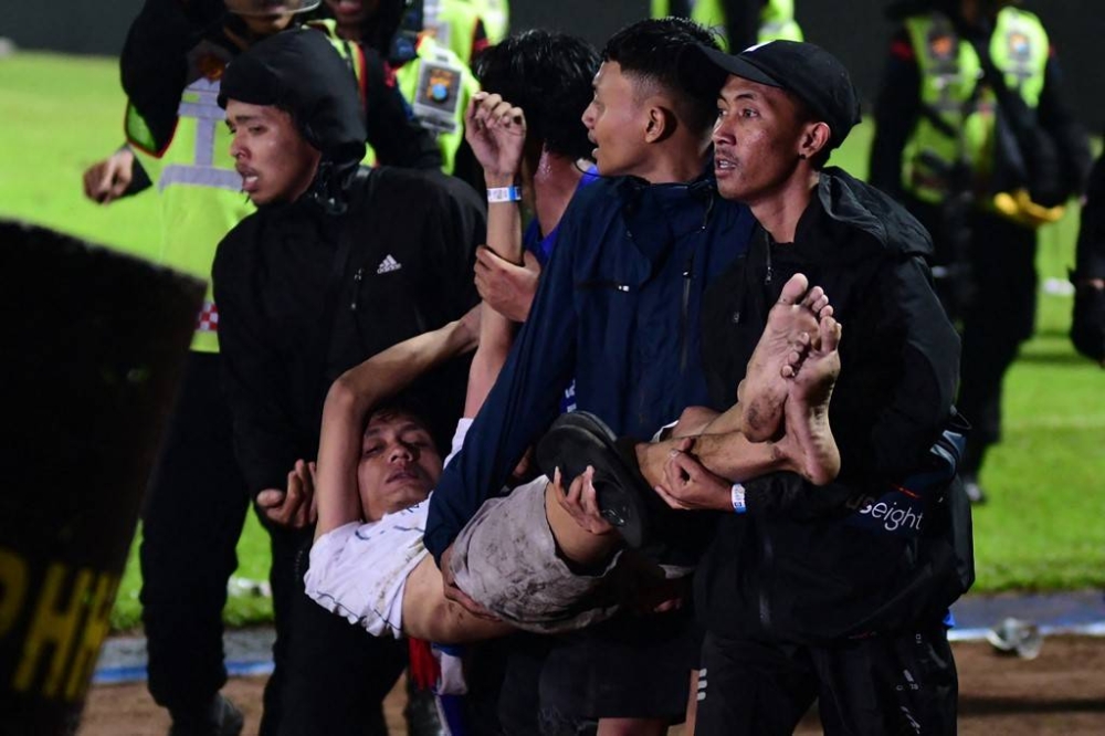 In this picture taken on October 1, 2022, a group of people carry a man at Kanjuruhan stadium in Malang, East Java. At least 127 people died at a football stadium in Indonesia late on October 1 when fans invaded the pitch and police responded with tear gas, triggering a stampede, officials said. — AFP pic