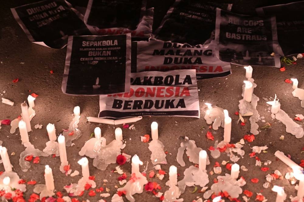 Banners reading ‘Indonesian football mourning’ are placed next to the candles as football supporters named Ultras spray flower petals during a candlelight vigil to show their condolences to victims of a stampede, in Jakarta on October 2, 2022.  — AFP pic