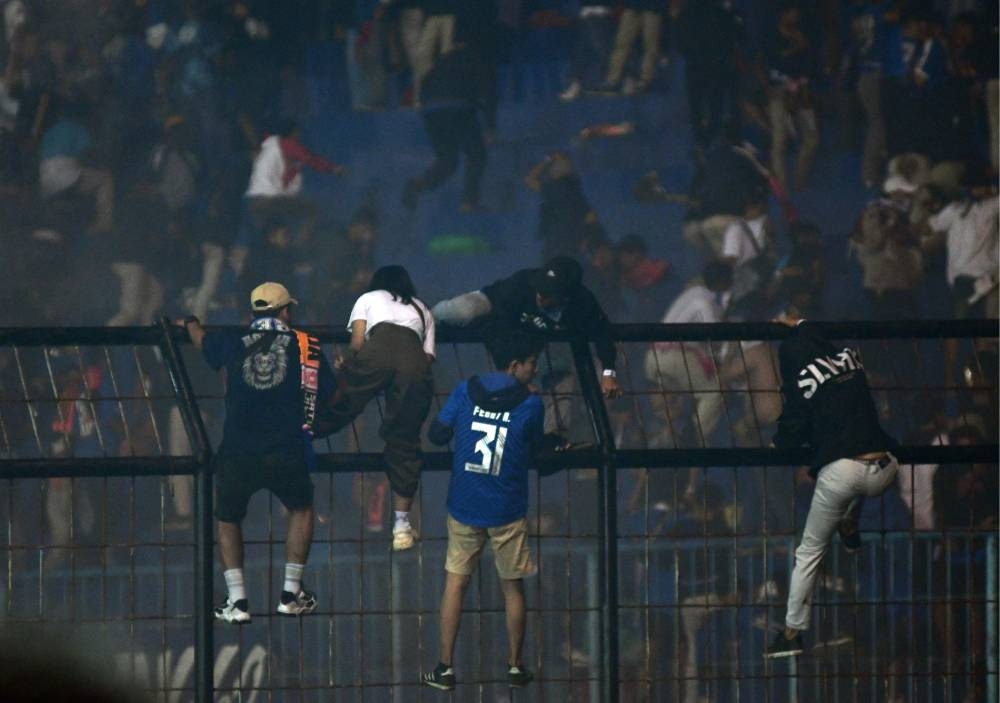This picture taken October 1, 2022 shows spectators climbing on a fence by the stands amid a deadly stampede after a football match between Arema FC and Persebaya at the Kanjuruhan stadium in Malang, East Java. — AFP pic 