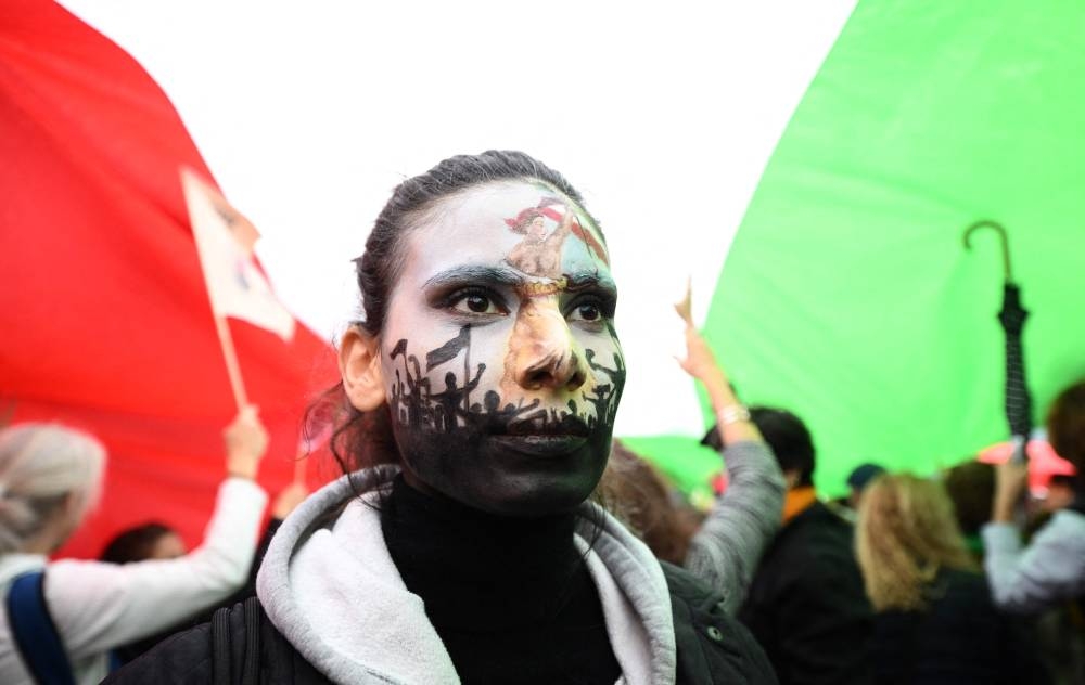 A protester wearing face-paint depicting France’s iconic ‘Marianne’ leading an uprising, stands under a giant Iranian flag as people gather in support of Kurdish woman Mahsa Amini during a protest October 2, 2022 on Place de la Republique in Paris, following her death in Iran. — AFP pic 