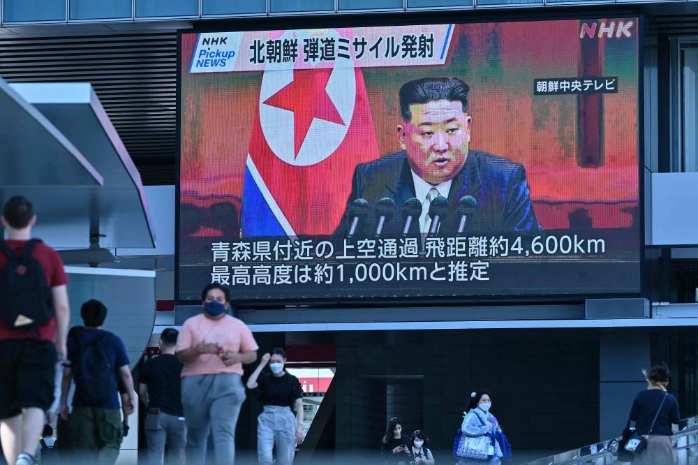 Pedestrians walk under a large video screen showing images of North Korea's leader Kim Jong-un during a news update in Tokyo on October 4, 2022, after North Korea launched a missile early in the day which prompted an evacuation alert when it flew over northeastern Japan. — AFP pic