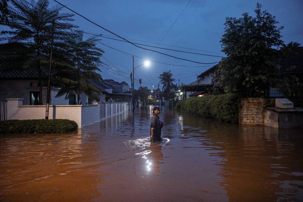 A man makes his way through a street flooded due to heavy rain in a residential area in Jakarta on October 6, 2022. — AFP pic