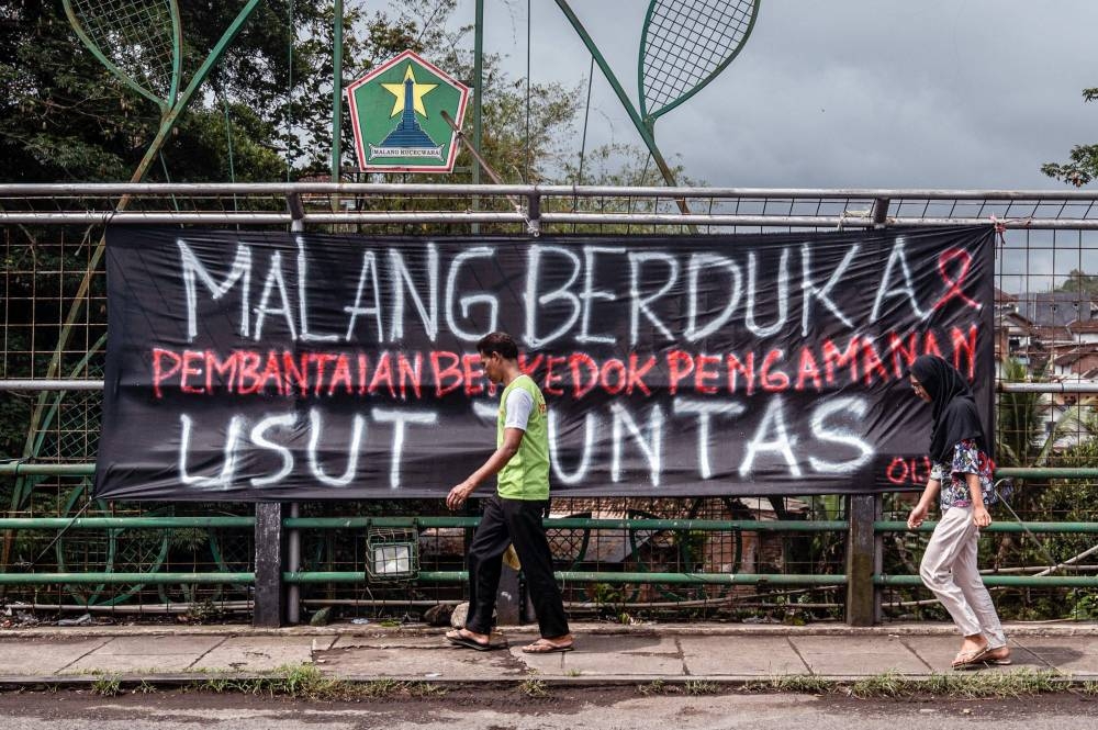 People walk past a banner placed in various places in Malang on October 6, 2022, as a call to investigate the stampede that killed at least 131 people in one of the deadliest disasters in football history. — AFP pic