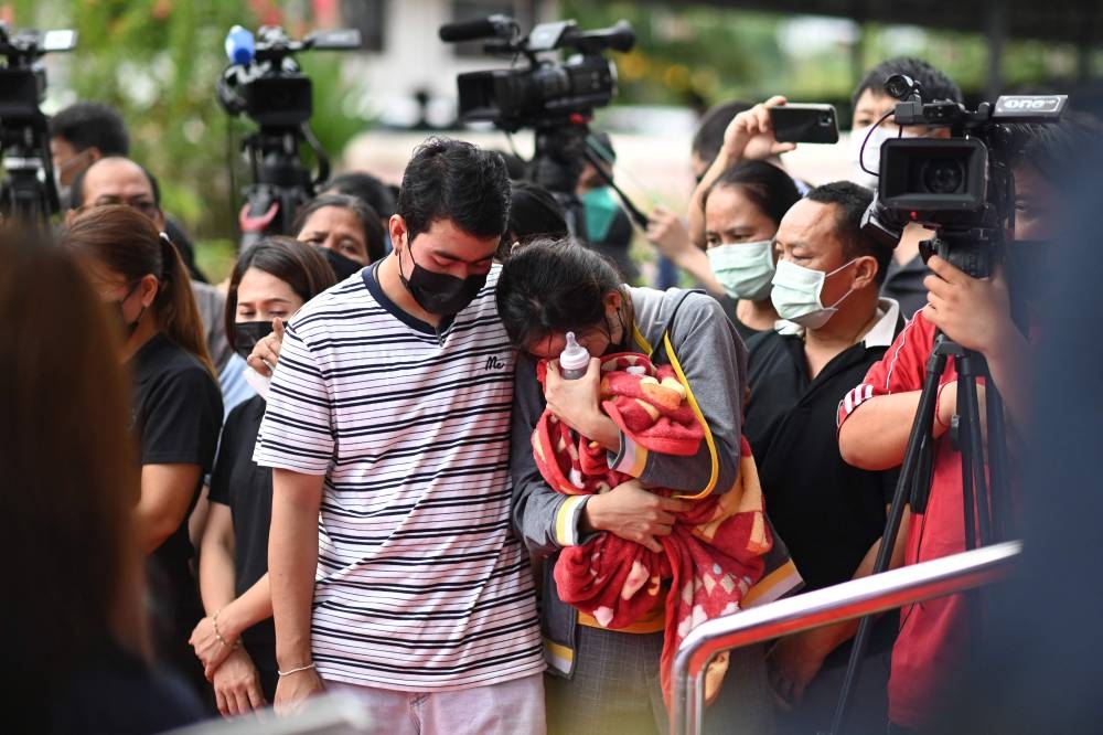 Sittipong Taothawong comforts his wife Kanjana Buakumchan as she holds their child's milk bottle and blanket while standing outside the nursery in Na Klang in Thailand's northeastern Nong Bua Lam Phu province on October 7, 2022, the day after a former police officer killed at least 37 people in a mass shooting at the site. — AFP pic