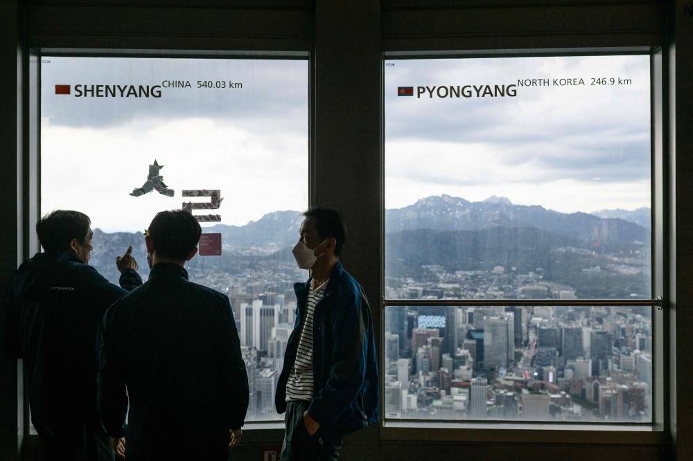 Visitors chat near a window (right) displaying the distance to the North Korean capital, Pyongyang, at the landmark Namsan Tower in Seoul on October 6, 2022.  — AFP pic