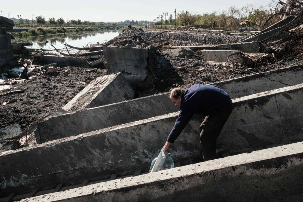 A man takes steps carefully while carrying water bottles as he crosses the destroyed bridge in the frontline town of Bakhmut in the Donetsk region on October 7, 2022, amid the Russian invasion of Ukraine. — AFP pic