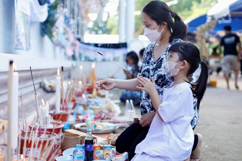 A woman and a girl light incense at the Wat Rat Samakee temple where coffins of victims are held, following a mass shooting in the town of Uthai Sawan, Nong Bua Lam Phu province, Thailand, October 8, 2022. — Reuters pic
