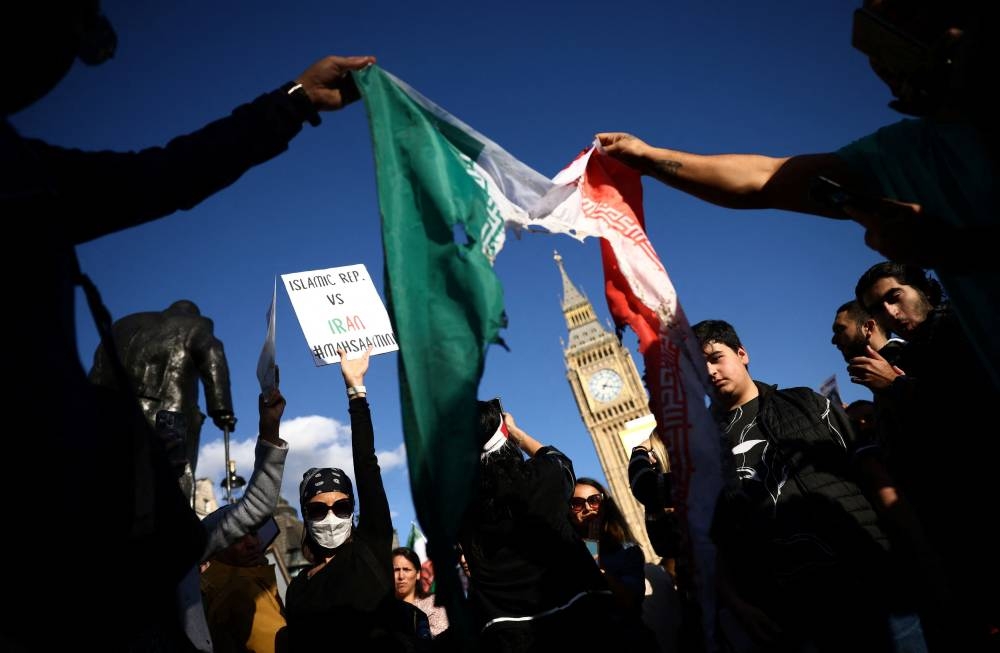 People hold a burnt Iranian flag outside the Houses of Parliament during a protest against the Islamic regime of Iran following the death of Mahsa Amini, in central London, Britain, October 8, 2022. — Reuters pic