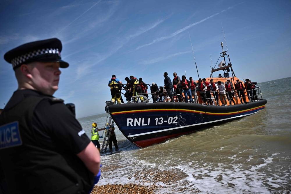 In this file photo taken on June 15, 2022 a British police officer stands guard on the beach of Dungeness, on the southeast coast of England, as Royal National Lifeboat Institution's (RNLI) members of staff help migrants to disembark from one of their lifeboat after they were picked up at sea while attempting to cross the English Channel.— AFP pic