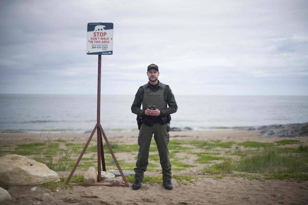 A bear patrol officer from conservatory of Manitoba, Ian Van Nest, stands next to a polar bear warning sign in Churchill, northern Canada, on August 7, 2022. — AFP pic