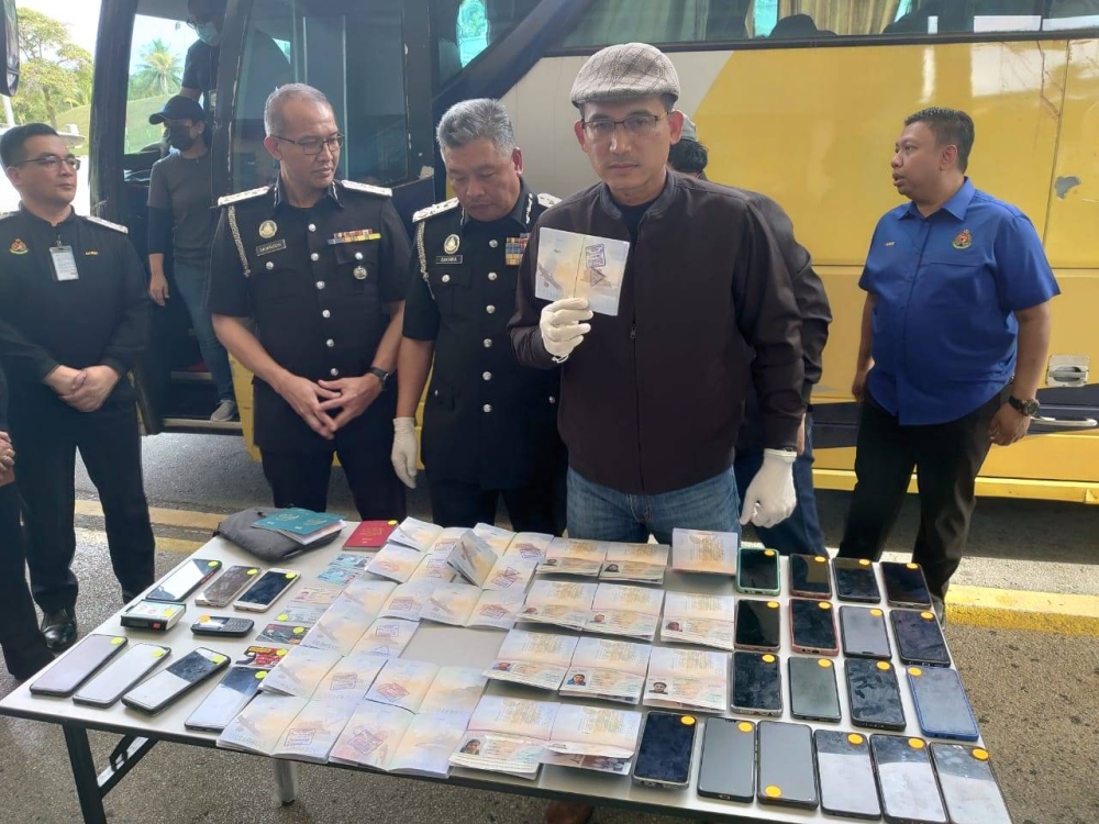 Immigration Department director-general Datuk Seri Khairul Dzaimee Daud (centre) shows a passport with fake stamps belonging to an undocumented migrant during a press conference at the Sultan Abu Bakar Complex in Helang Patah, Iskandar Puteri, October 12, 2022. — Picture by Ben Tan