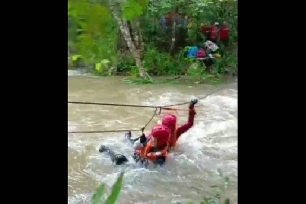 A Fire and Rescue Department personnel helps a hiker across the river during the rescue operations at Telaga Tujuh waterfalls in Langkawi October 16, 2022. — Video screencap via Twitter/Bernama