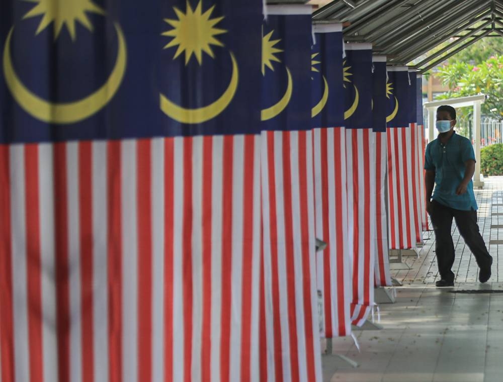 A man walks past Malaysian flags in Ipoh August 31, 2022. Our country is more than 60 years old but we still can’t seem to shed the divisive racial-religious rhetoric. — Picture by Farhan Najib