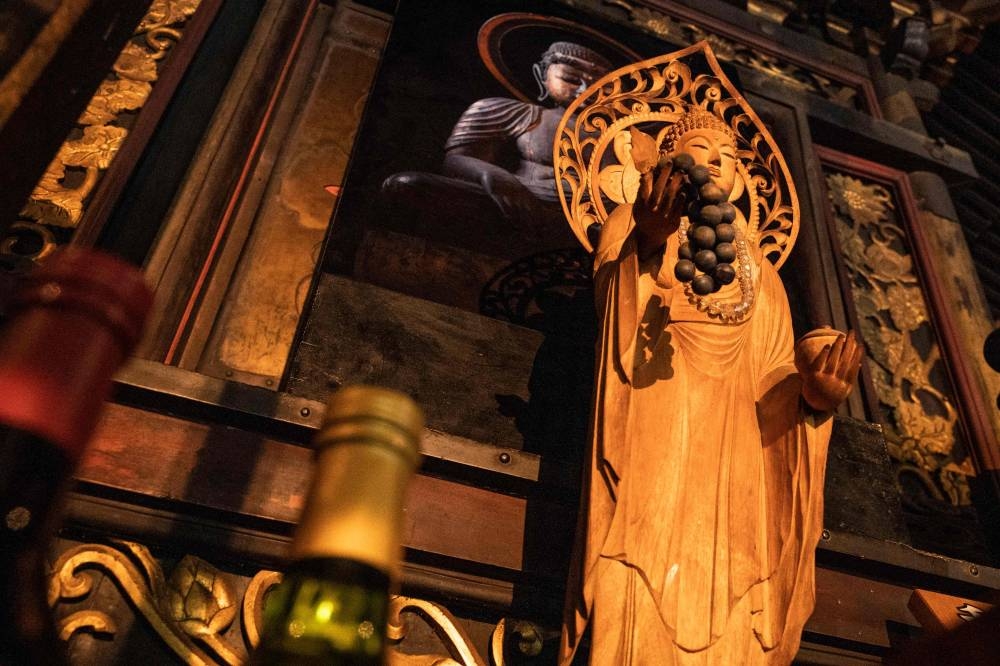 A wooden statue holding grapes in front of a picture of an ancient statue holding grapes – which is only shown to the public every five years – inside Daizenji temple, nicknamed the 