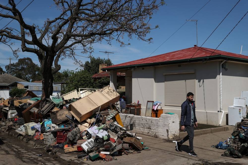A pedestrian walks past piles of debris lining a residential street following severe flooding and damage to homes in the Maribyrnong suburb of Melbourne October 17, 2022. — Reuters pic