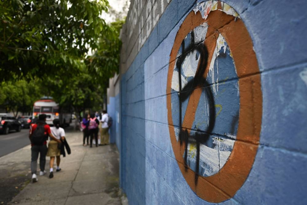 Students walk next to a wall painted with an anti-bitcoin protest symbol, in San Salvador, on October 18, 2022. — AFP pic