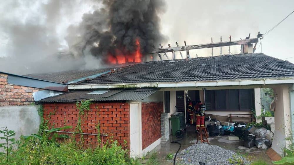Sarawak Bomba personnel are pictured entering one of the houses in Kenyalang Park to begin the firefighting operation. — Borneo Post pic