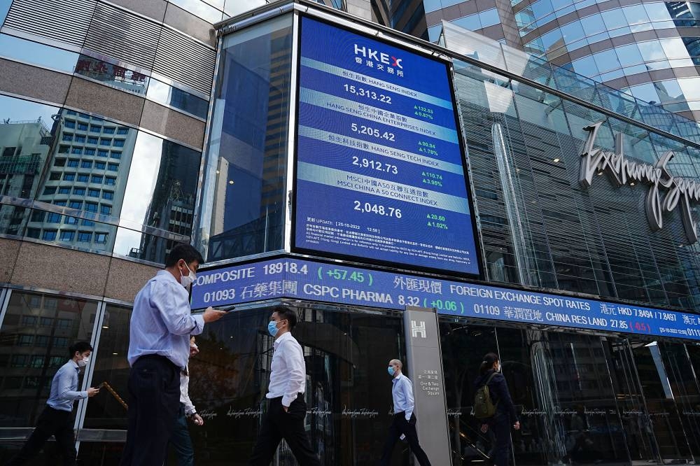People walk past a screen displaying the Hang Seng stock index at Central district, in Hong Kong, China October 25, 2022. — Reuters pic