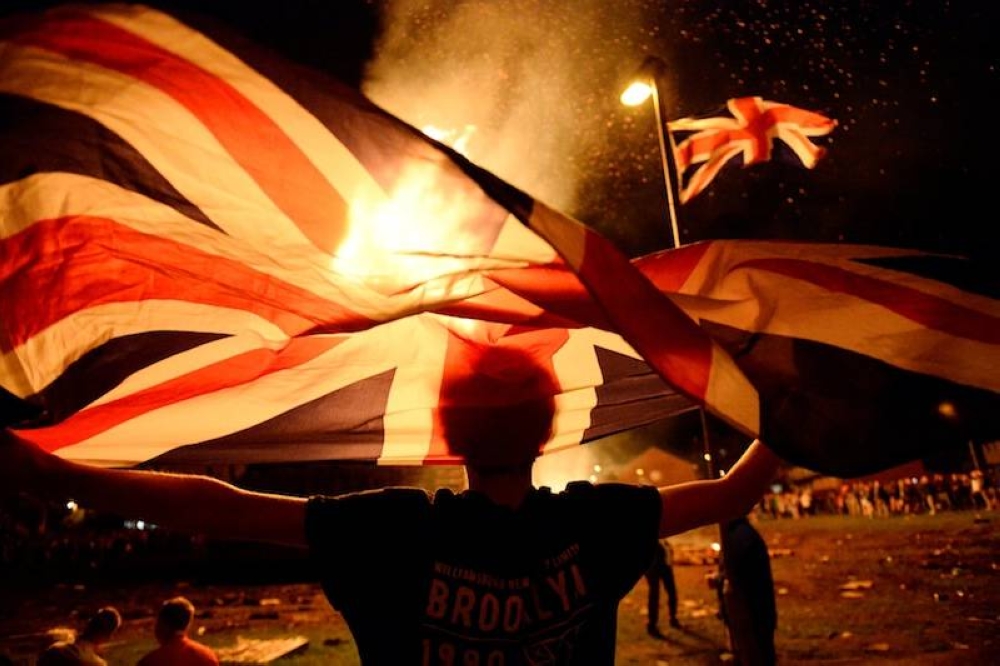 A boy holds a Union Jack flag in front of a bonfire burning in the Shankill Road area in Belfast, Northern Ireland, July 12, 2016. — Reuters pic