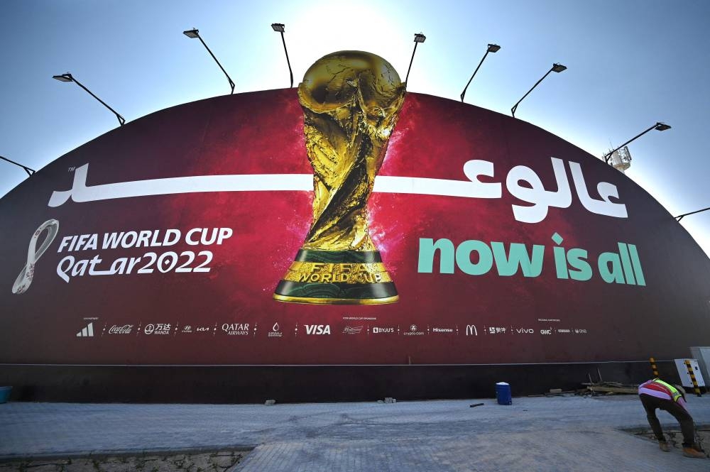 A man works in front of a Qatar 2022 Fifa World Cup football tournament billboard in Doha on October 29, 2022. — AFP pic