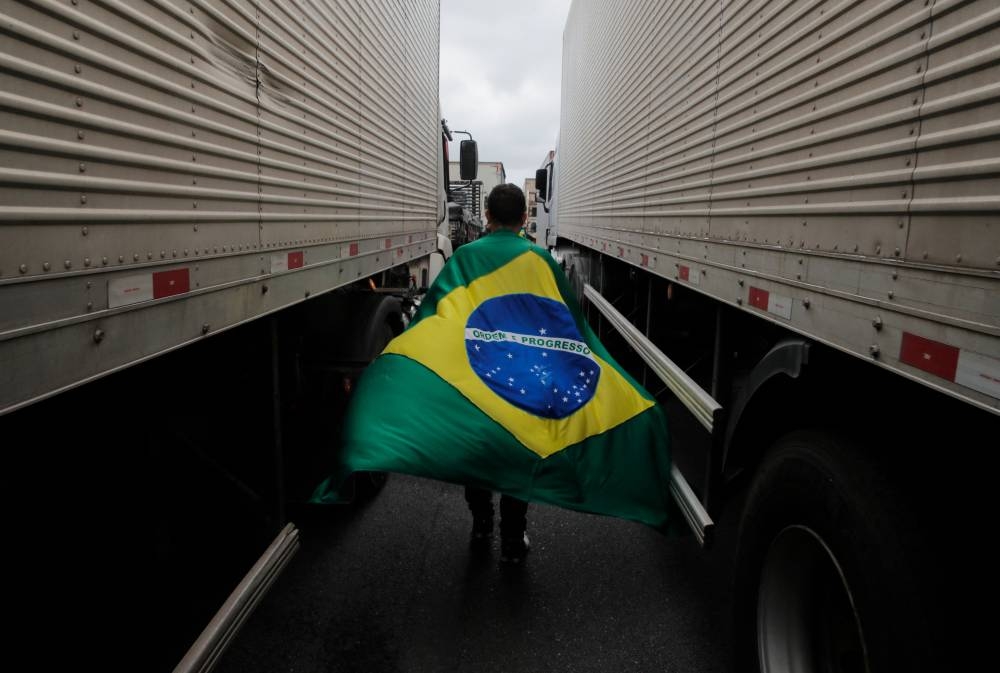 A supporter of President Jair Bolsonaro with a Brazilian flag walks between trucks during a blockade on Castelo Branco highway, on the outskirts of Sao Paulo November 1, 2022. — AFP pic 