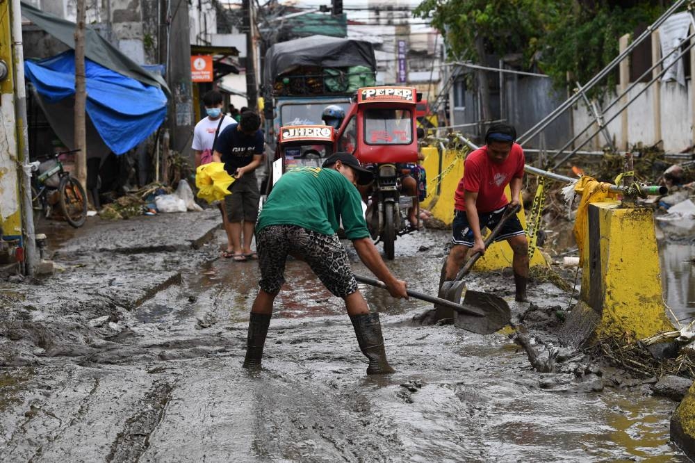 Residents shovel mud along a street in Noveleta town, Cavite province on October 31, 2022, after Tropical Storm Nalgae hit the region. ― AFP pic