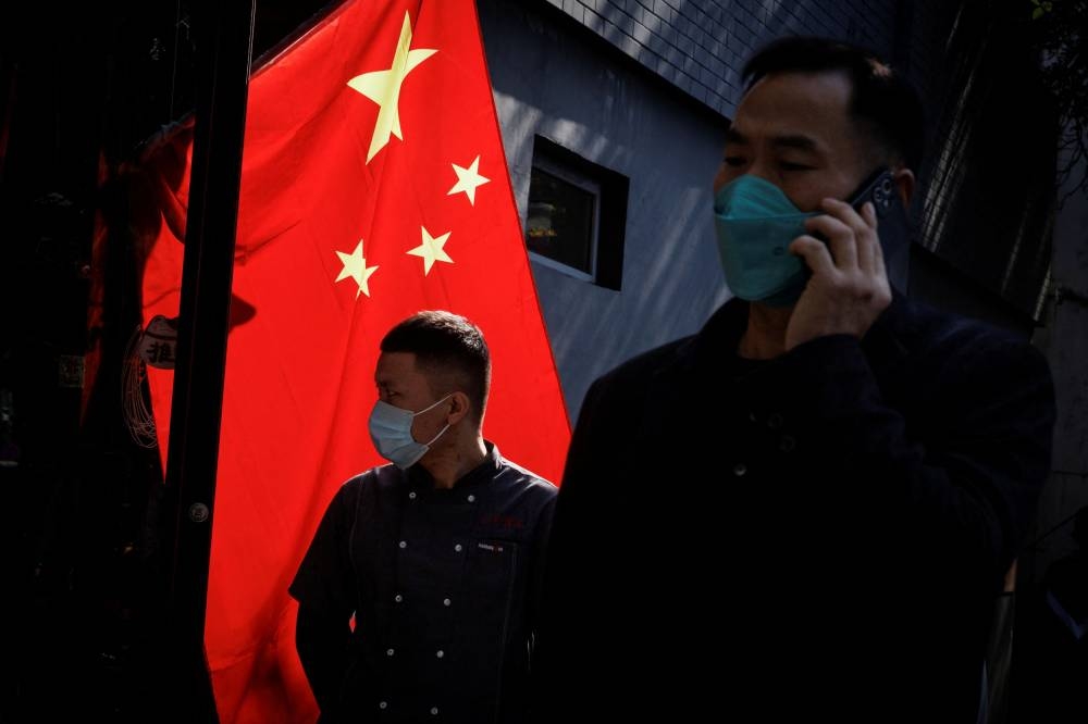 People wearing masks walk past a Chinese national flag as outbreaks of coronavirus disease (COVID-19) continue in Beijing November 3, 2022. — Reuters pic