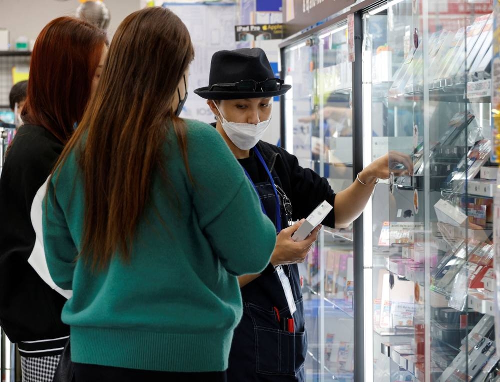 A clerk shows a used iPhone to customers from Thailand in Iosys Corp's shop selling used smartphones at Akihabara electronics district in Tokyo October 28, 2022. — Reuters pic