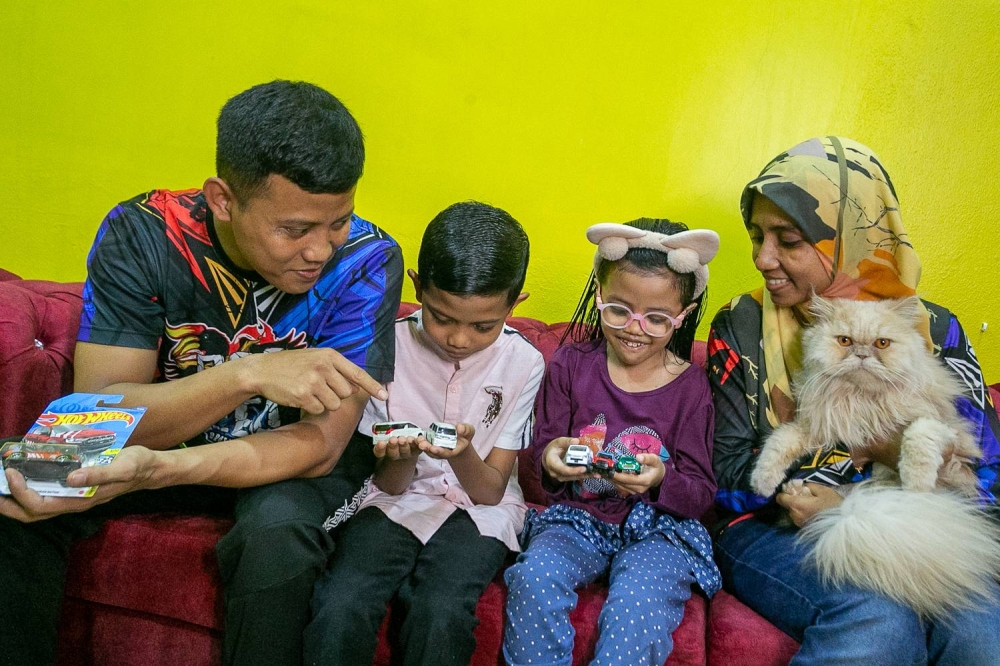 Mohd Ariffin Sokher (left) with his family looking at some of the die-cast cars he redesigned at his home in Alor Gajah on November 6, 2022 --- Photo by Raymond Manuel