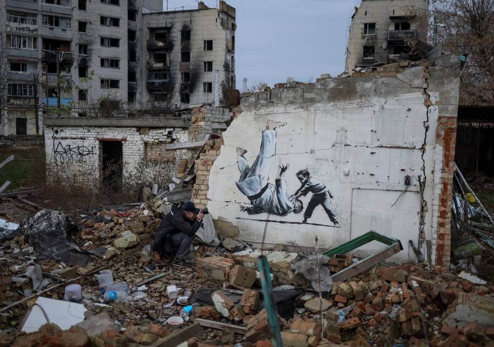 A photographer takes a picture of a new graffiti in Banksy's signature style, although not posted by the mercurial artist on social media, in the Ukrainian town of Borodianka, which had been occupied by Russia until April and heavily damaged by fighting in the early days of Russian invasion, November 12, 2022. ― Reuters pic