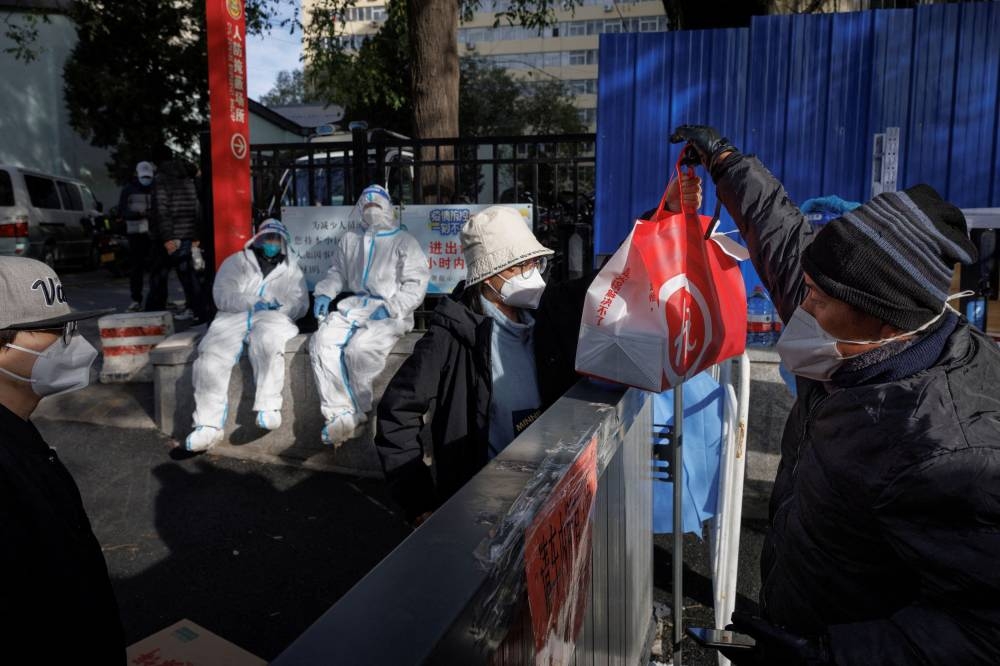 A delivery driver hands food to a resident of an apartment compound that was placed under lockdown as outbreaks of the coronavirus disease (Covid-19) continue in Beijing, China, November 12, 2022. — Reuters pic