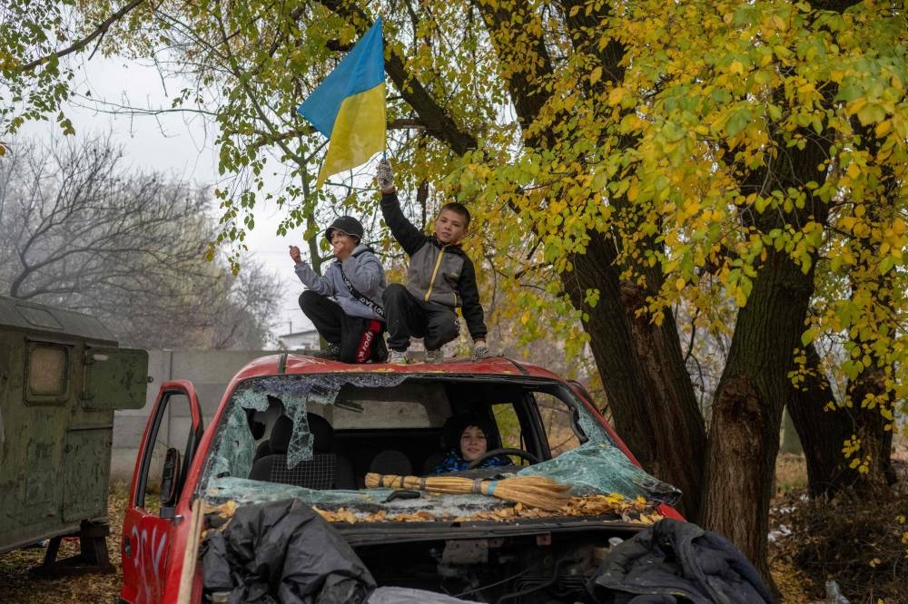 A young boy stands on a destroyed car, waving a Ukrainian flag, at a former Russian checkpoint at the entrance of Kherson as local residents celebrate the liberation of the city, on November 13, 2022, amid Russia's invasion of Ukraine. — AFP pic