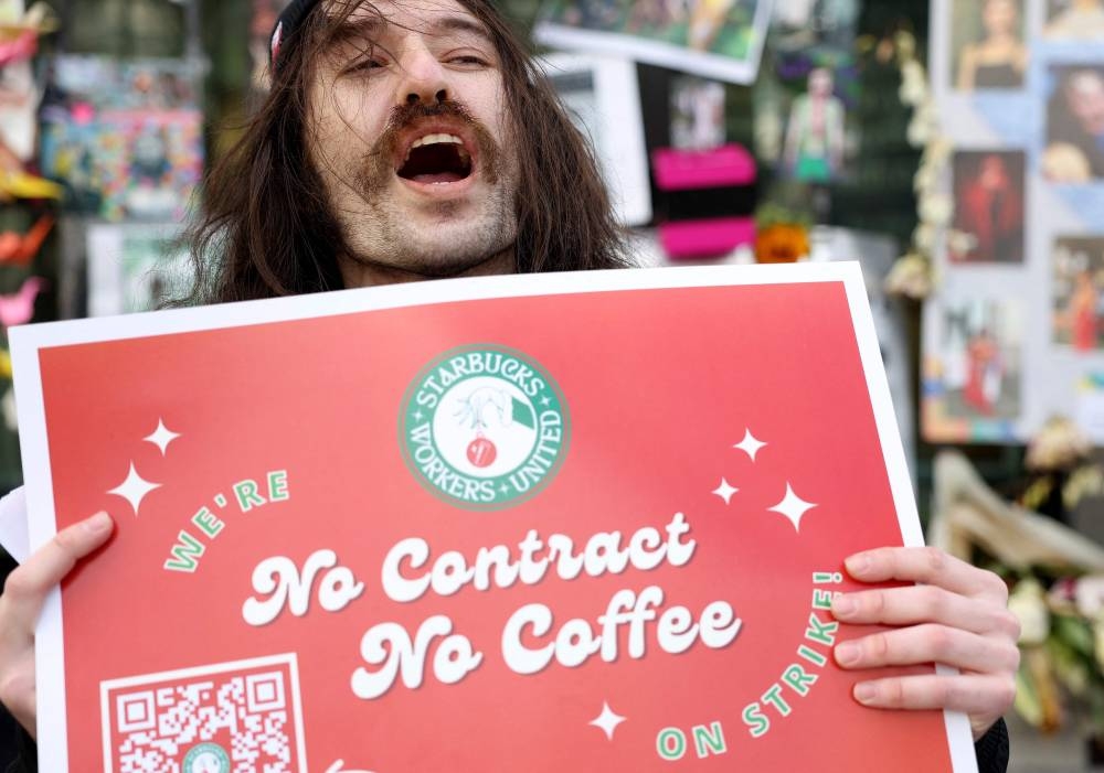 Striking Starbucks worker Kyle Trainer holds a sign outside of a Starbucks coffee shop during a national strike in San Francisco November 17, 2022. — AFP pic 