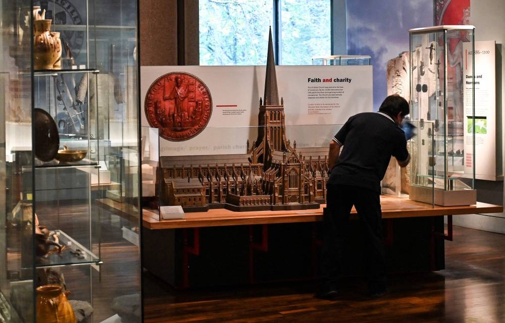 A cleaner wipes down a glass covering the miniature of a gothic church displayed at the Museum of London, in London on November 8, 2022. — AFP pic