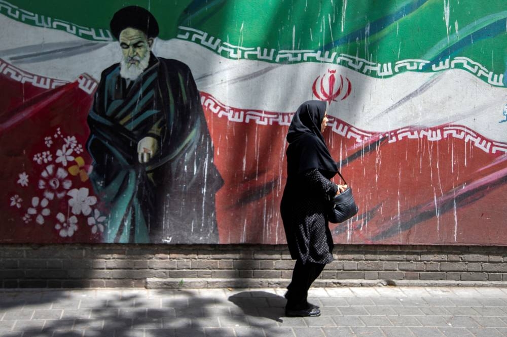 An Iranian woman walks in front of a mural of Iran's late leader Ayatollah Ruhollah Khomeini in Tehran, Iran.  — Reuters pic