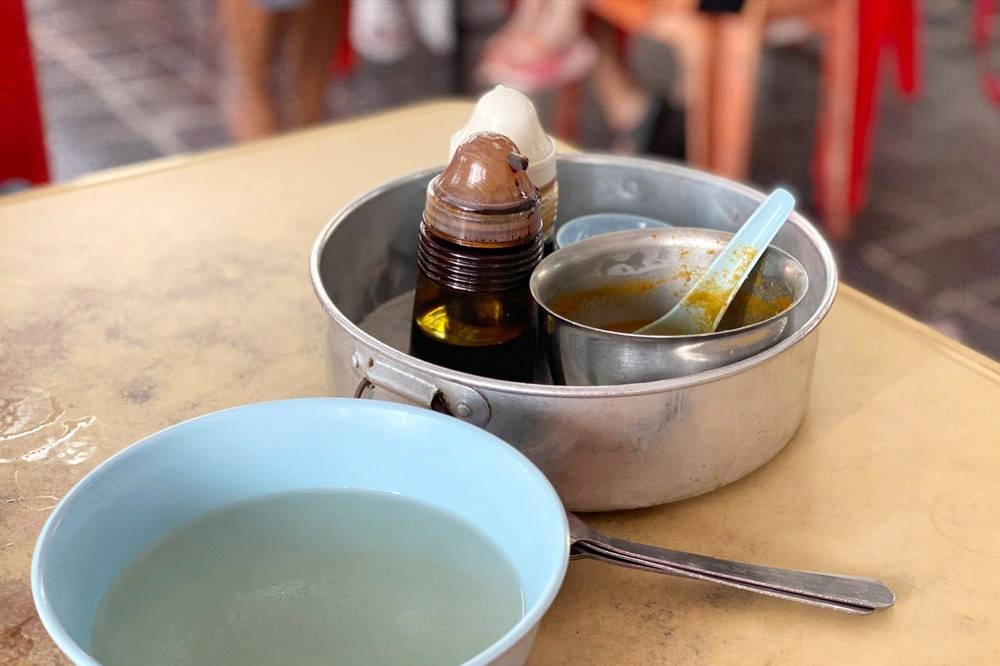 A round tray of condiments is served alongside a bowl of soup while you wait for your chicken rice.