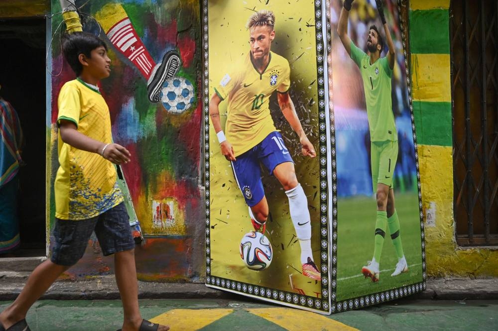 A boy walks past a wall decorated posters showing Brazil's footballer Alisson Becker and Neymar Jr playing in Qatar 2022 World Cup, in Kolkata on November 28, 2022. — Reuters pic