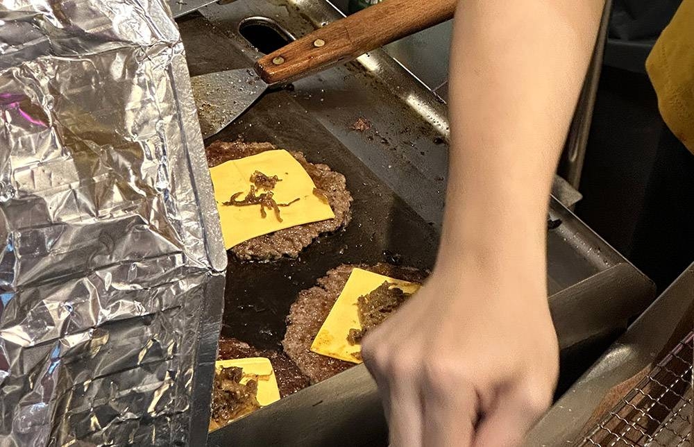 Once the patties are cooked, they add cheese and onions on top.