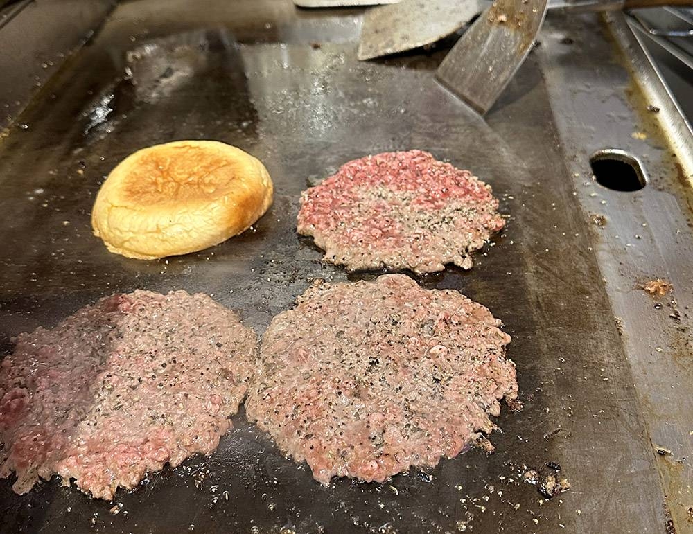 The minced meat patty is shaped like a ball and smashed on the hot griddle with a flat spatula.