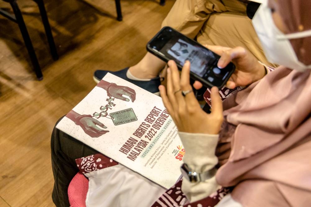 A woman takes a picture of a copy of Suaram's Human Rights Report 2022 at the Kuala Lumpur and Selangor Chinese Assembly Hall December 6, 2022. — Picture by Firdaus Latif