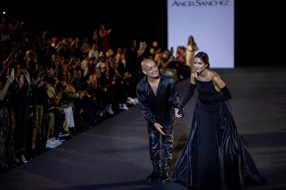Venezuelan designer Angel Sanchez accompanied by a model, salutes on stage after presenting his collection. ― AFP pic