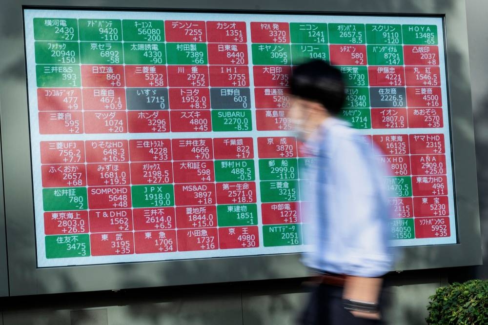 A man walks past an electronic board showing the values of various companies trading on the Tokyo Stock Exchange, along a street in Tokyo on December 7, 2022. — AFP pic